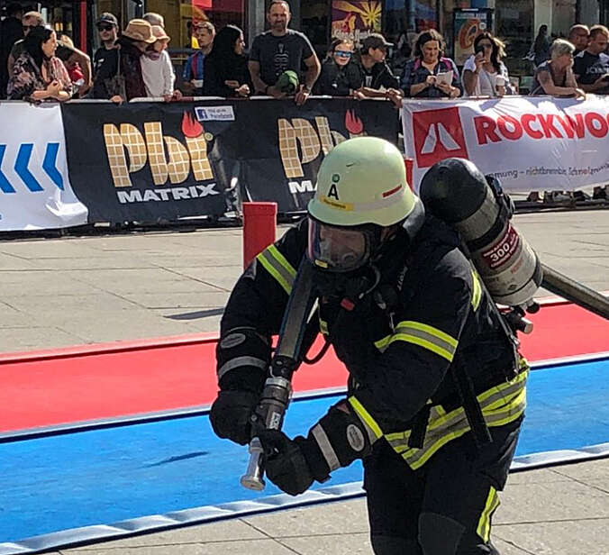 Feuerwehrmann mit Atemschutz zieht Schlauchleitung bei Leistungswettbewerb vor Publikum
