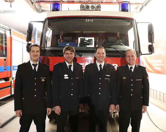 Vier Feuerwehrmänner stehen vor Feuerwehrauto