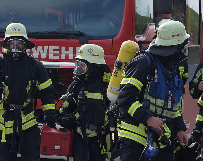 Feuerwehrmänner mit Helmen und Masken vor dem Feuerwehrauto