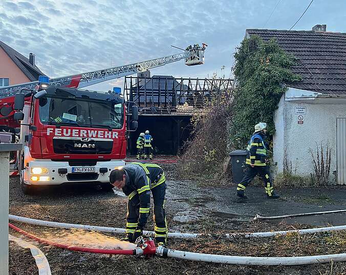 Feuerwehrfahrzeug mit mehreren Feuerwehrkräften vor abgebranntem Schuppen