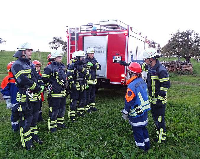 Feuerwehrangehörige stehen hinter einem Feuerwehrfahrzeug